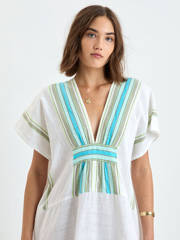 Close up on a Woman wearing lemlem GASIRA Caftan featuring a chic stripe pattern in aqua blue and sage tones, delineated by dark olive dots and accented with a splash of neon yellow on a cream background
