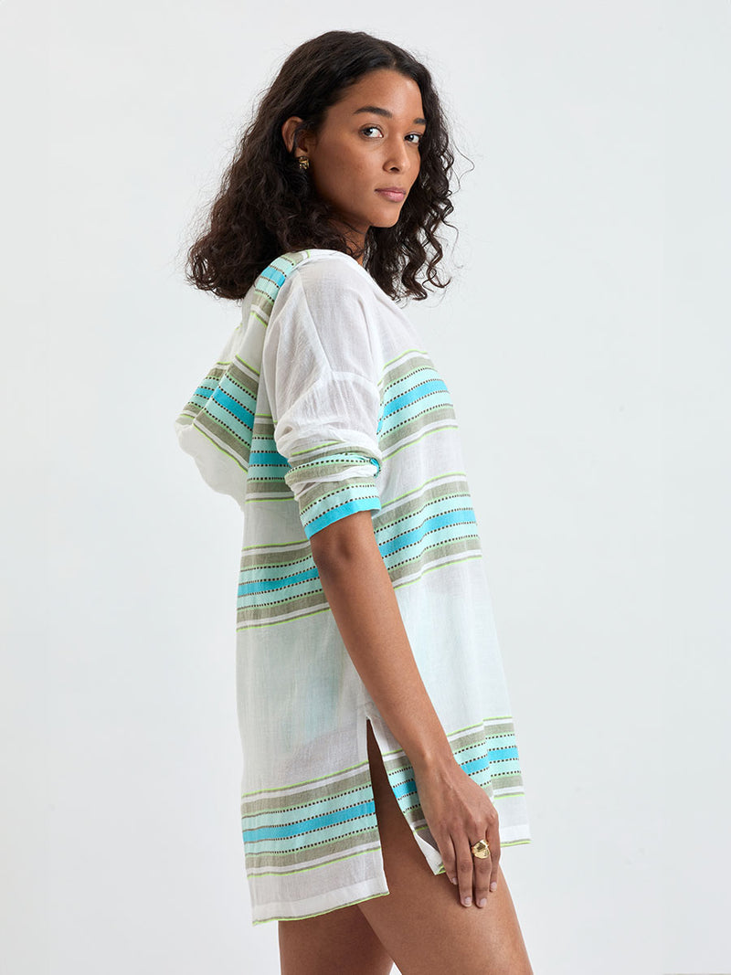 Side shot of a Woman wearing lemlem HENOK Hoodie featuring a chic stripe pattern in aqua blue and sage tones, delineated by dark olive dots and accented with a splash of neon yellow on a cream background 