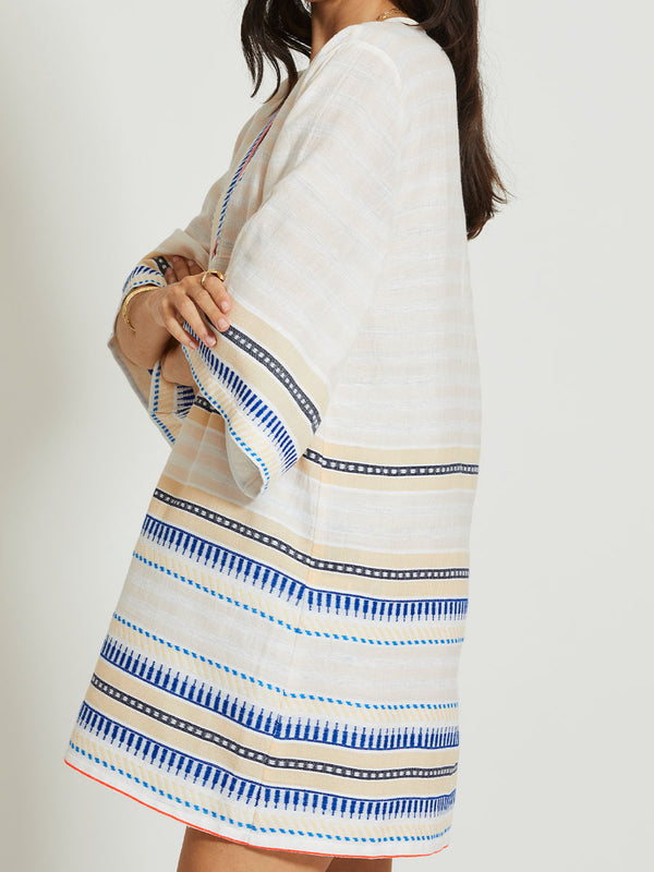 Clos eup on a Woman Standing Wearing lemlem BELKIS | V Neck Caftan featuring a soft shadow stripe base with graphic Tibeb-inspired bands in rich blues, black, and vanilla on a creamy white ground