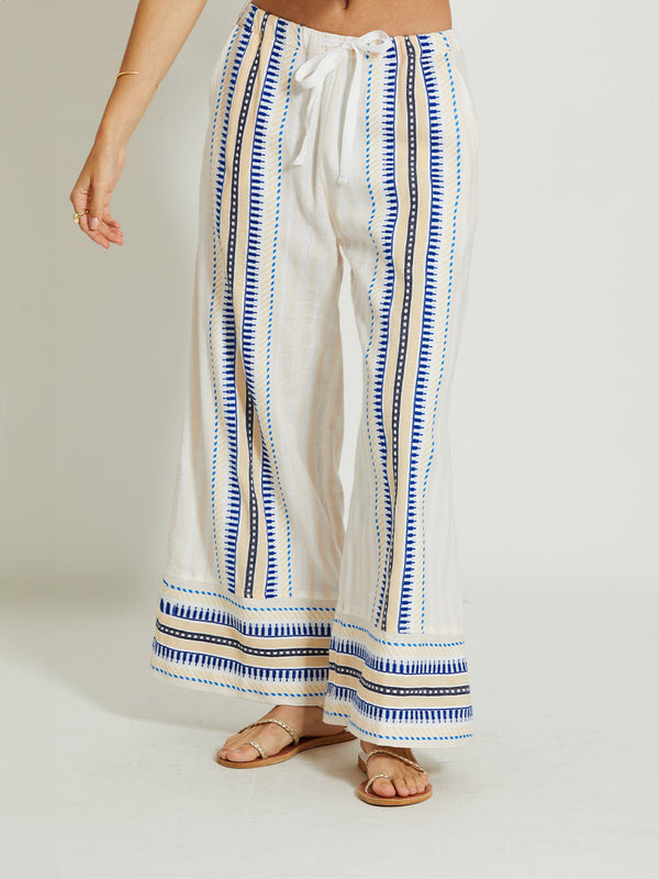 Close up on a Woman Standing Wearing lemlem DESTA | Pants featuring a soft shadow stripe base with graphic Tibeb-inspired bands in rich blues, black, and vanilla on a creamy white ground