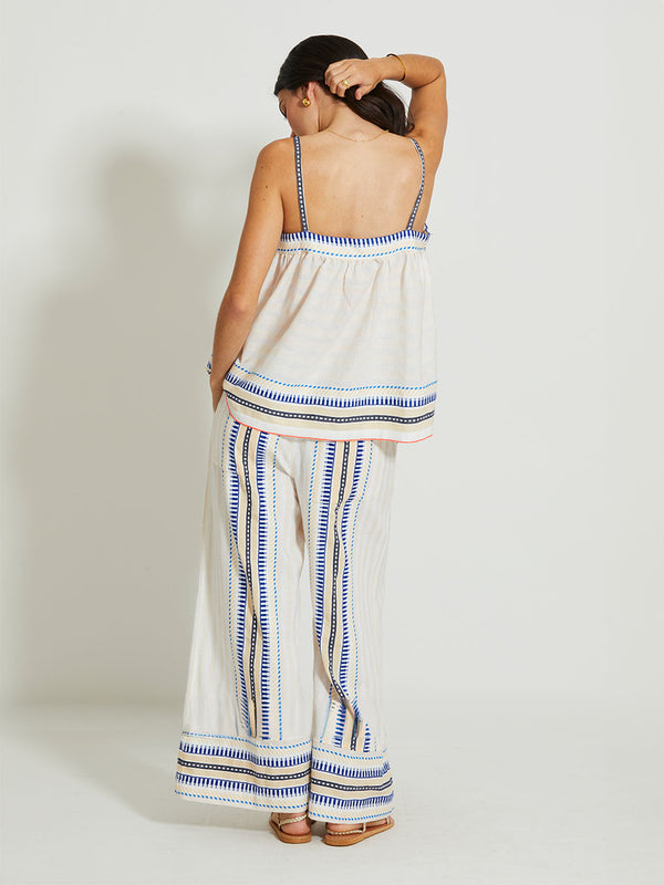 Back of a Woman Standing Wearing lemlem THEA | Tank Top featuring a soft shadow stripe base with graphic Tibeb-inspired bands in rich blues, black, and vanilla on a creamy white ground