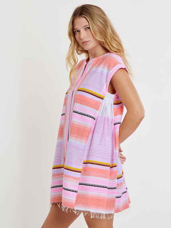 Woman standing wearing lemlem handwoven  ELINA Caftan featuring intricate stripe pattern interlaced with delicate mini Tibeb detailing, expressed in a soft yet vivid palette of cool pink, warm tangerine, rose, orchid, and accents of peach and deep burgundy.