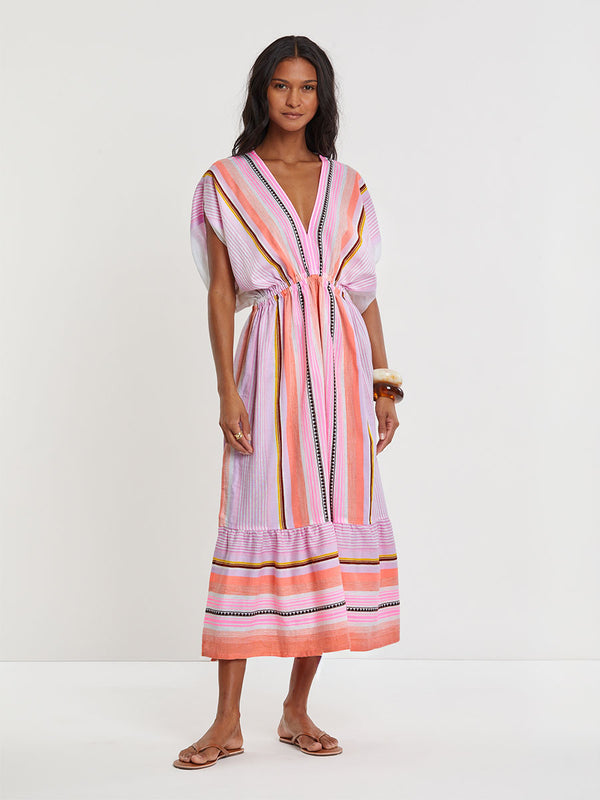  Woman standing wearing lemlem handwoven  LEILA Dress featuring intricate stripe pattern interlaced with delicate mini Tibeb detailing, expressed in a soft yet vivid palette of cool pink, warm tangerine, rose, orchid, and accents of peach and deep burgundy.
