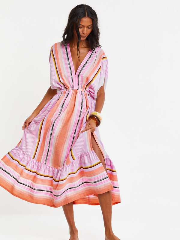 Woman standing wearing lemlem handwoven  LEILA Dress featuring intricate stripe pattern interlaced with delicate mini Tibeb detailing, expressed in a soft yet vivid palette of cool pink, warm tangerine, rose, orchid, and accents of peach and deep burgundy.