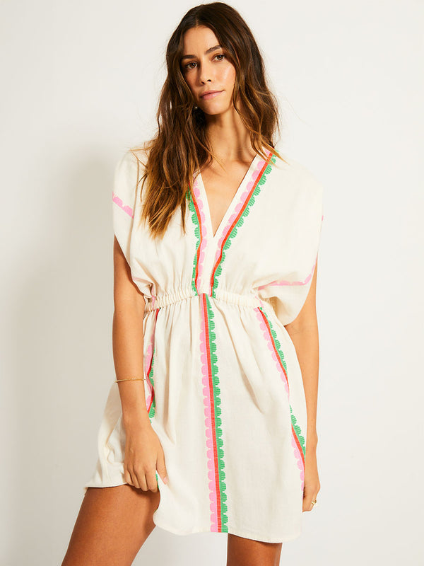 Woman Standing Wearing lemlem ALEM Plunge Dress featuring a playful, preppy scalloped Tibeb weave with vibrant green, soft pink, and fiery red accents.
