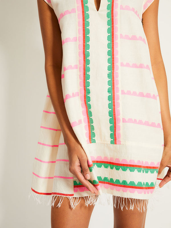 Close up on a Woman Standing Wearing lemlem ELINA Caftan featuring a playful, preppy scalloped Tibeb weave with vibrant green, soft pink, and fiery red accents
