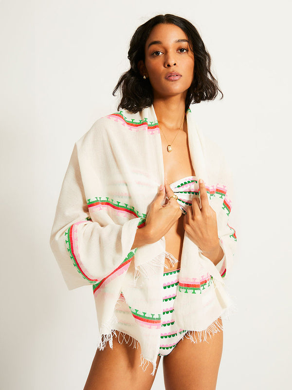 Woman Standing Wearing lemlem LEMA Sarong featuring a playful, preppy scalloped Tibeb weave with vibrant green, soft pink, and fiery red accents and matching bikini set
