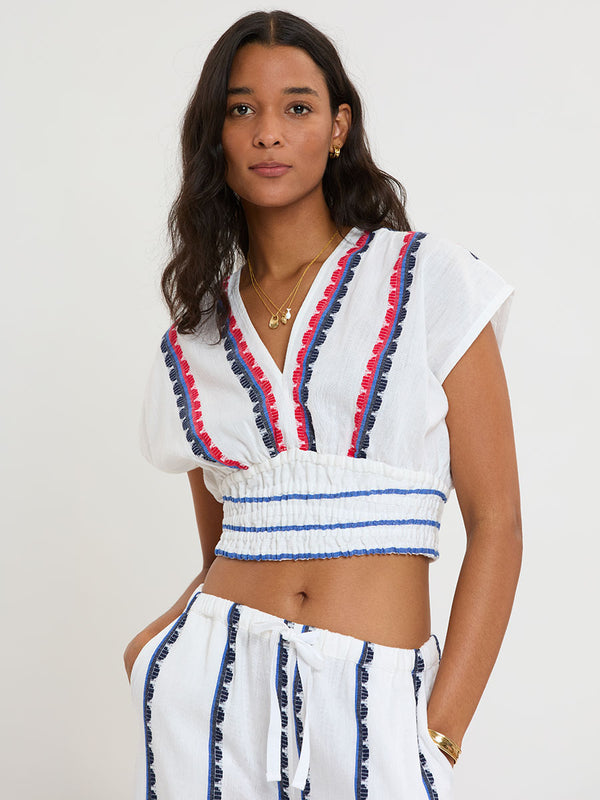 Woman Standing wearing lemlem handwoven ALIA Plunge Top and DESTA Pants featuring a playful, preppy scalloped Tibeb weave with classic navy, red, and vibrant blue accents.