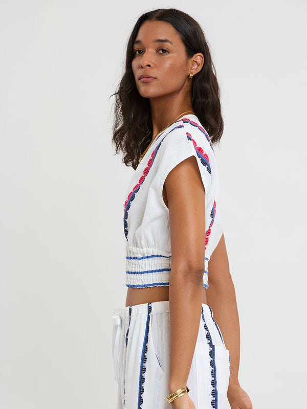 Woman Standing wearing lemlem handwoven ALIA Plunge Top and DESTA Pants featuring a playful, preppy scalloped Tibeb weave with classic navy, red, and vibrant blue accents.