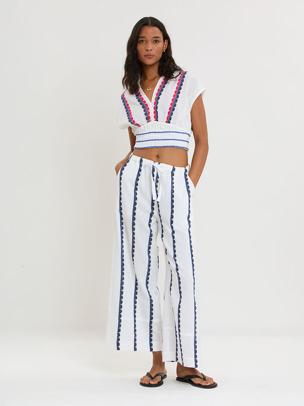 Woman Standing wearing lemlem handwoven DESTA Pants and AVA Bandeau Bikini Top featuring a playful, preppy scalloped Tibeb weave with classic navy, red, and vibrant blue accents.