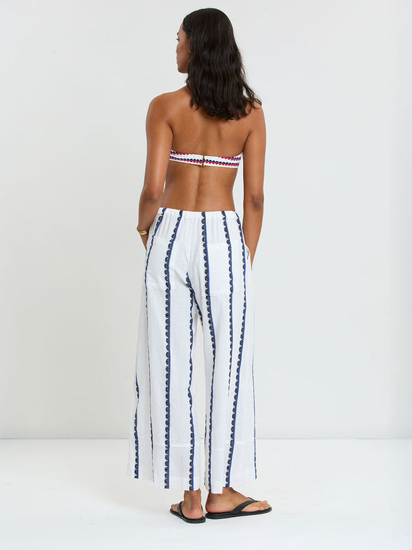 Woman Standing wearing lemlem handwoven DESTA Pants and AVA Bandeau Bikini Top featuring a playful, preppy scalloped Tibeb weave with classic navy, red, and vibrant blue accents.