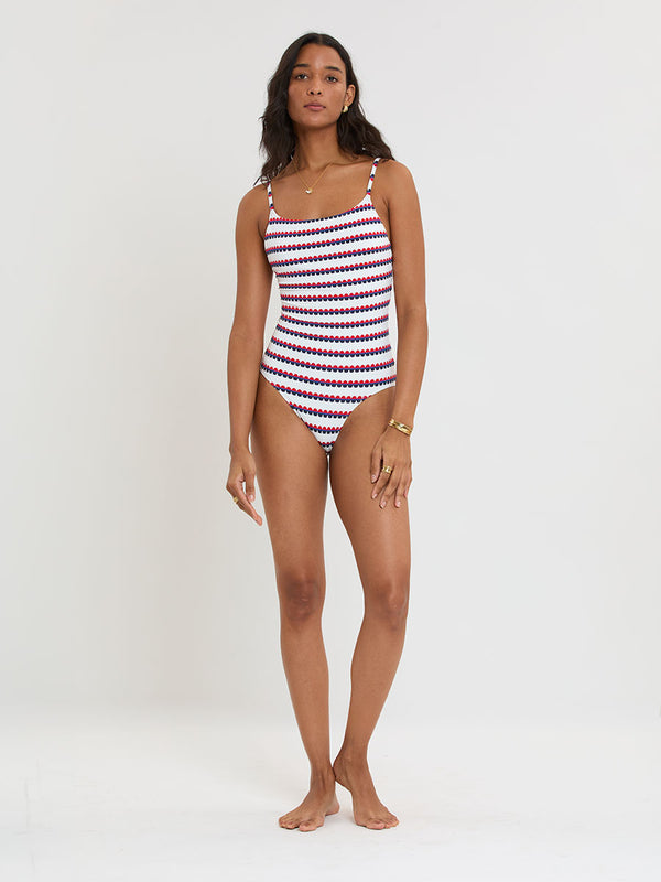Woman Standing wearing lemlem ELENE One Piece featuring a playful, preppy scalloped Tibeb weave with classic navy, red, and vibrant blue accents.