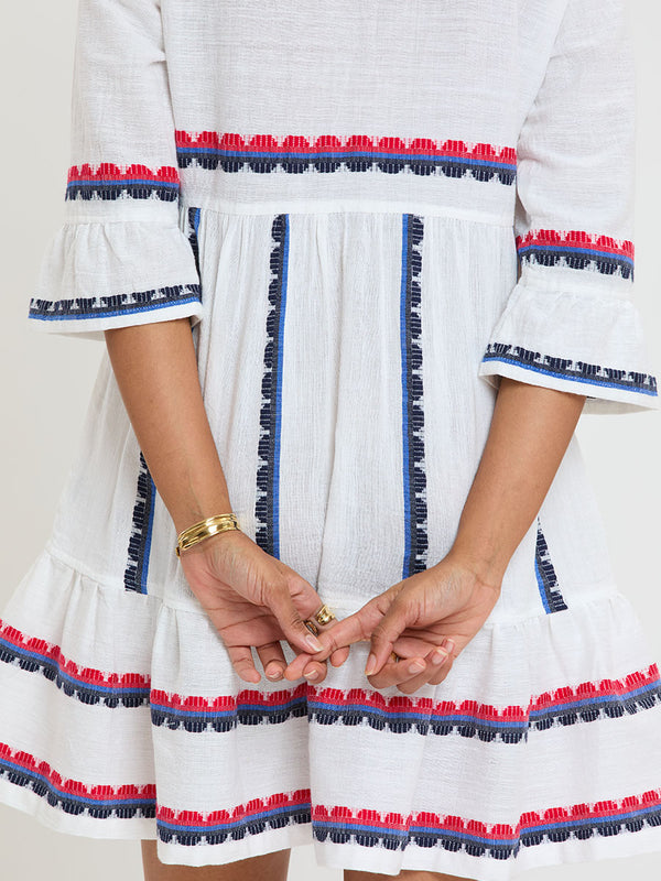 Close up on a Woman Standing wearing lemlem handwoven HANNA Dress featuring a playful, preppy scalloped Tibeb weave with classic navy, red, and vibrant blue accents.
