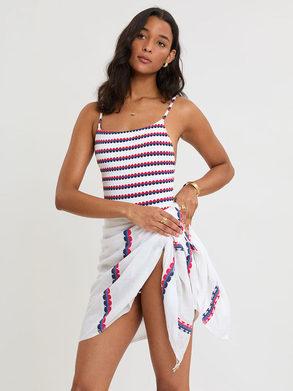 Woman Standing wearing lemlem ELENE One Piece and LEMA Sarong featuring a playful, preppy scalloped Tibeb weave with classic navy, red, and vibrant blue accents.