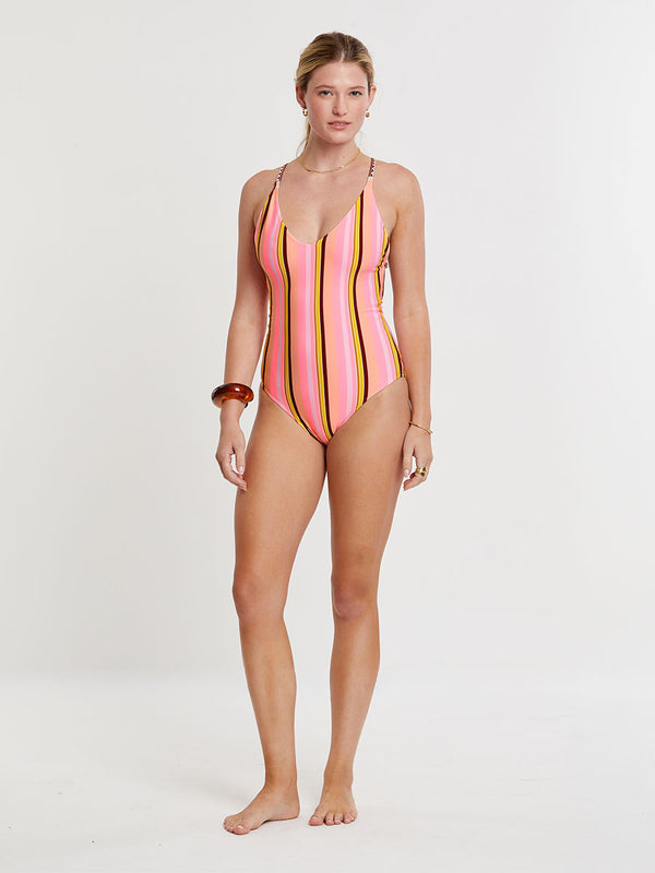 Woman Standing wearing lemlem RETIRO One Piece featuring intricate stripe pattern interlaced with delicate mini Tibeb detailing, expressed in a soft yet vivid palette of cool pink, warm tangerine, rose, orchid, and accents of peach and deep burgundy.