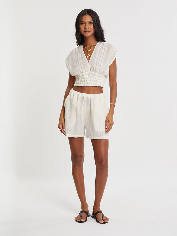 Woman standing wearing lemlem handwoven ALEM Plunge Top and SAFIA Shorts  featuring extra light gauzy cotton in a delicate cream color.