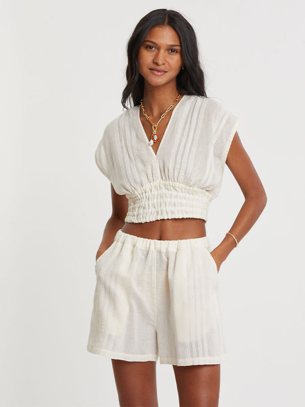 Woman standing wearing lemlem handwoven ALEM Plunge Top and SAFIA Shorts  featuring extra light gauzy cotton in a delicate cream color.