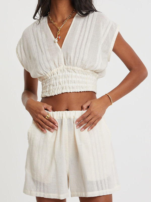 Woman standing wearing lemlem handwoven ALEM Plunge Top and SAFIA Shorts  featuring extra light gauzy cotton in a delicate cream color.