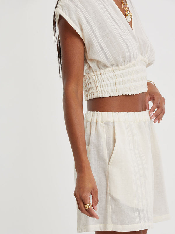 Woman standing wearing lemlem handwoven ALEM Plunge Top and SAFIA Shorts  featuring extra light gauzy cotton in a delicate cream color.