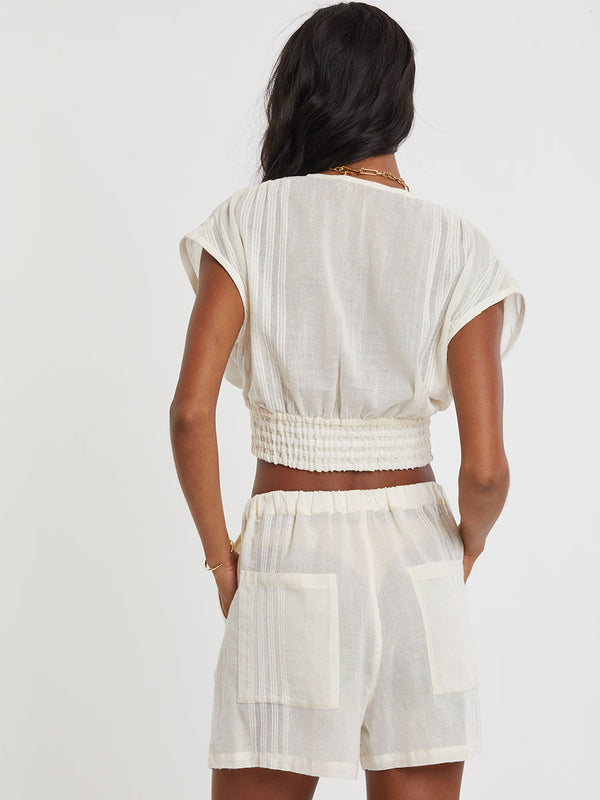 Woman standing wearing lemlem handwoven ALEM Plunge Top and SAFIA Shorts  featuring extra light gauzy cotton in a delicate cream color.