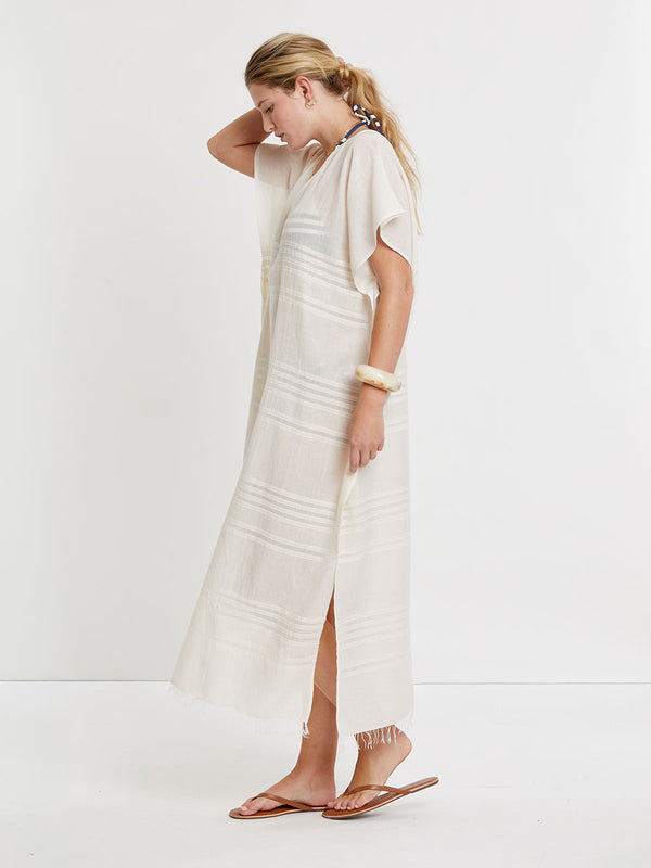 Woman standing wearing lemlem handwoven DALILA Caftan featuring extra light gauzy cotton in a delicate cream color.