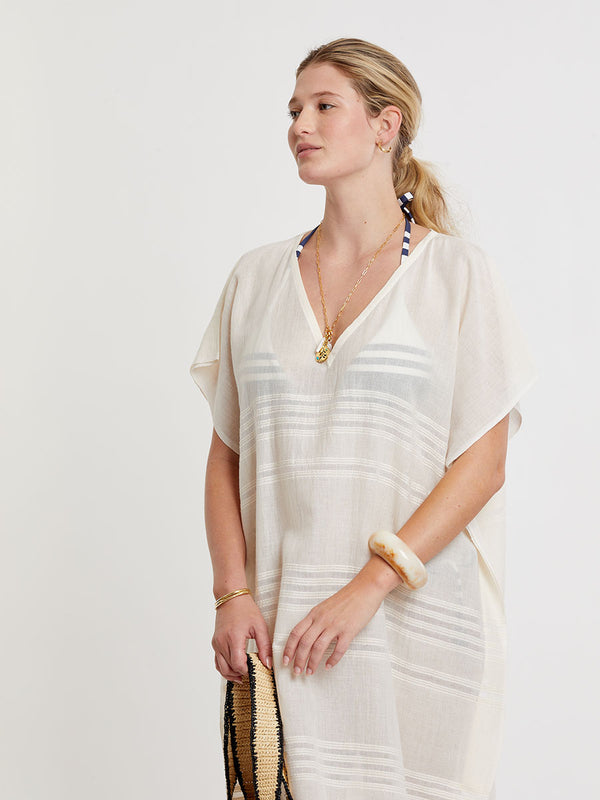 Woman standing wearing lemlem handwoven DALILA Caftan featuring extra light gauzy cotton in a delicate cream color.