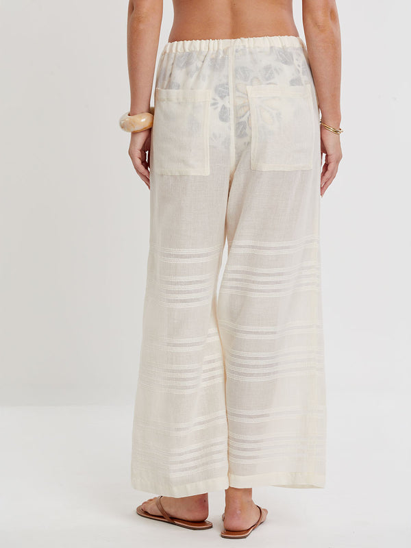Woman standing wearing lemlem handwoven DESTA Pants featuring extra light gauzy cotton in a delicate cream color.