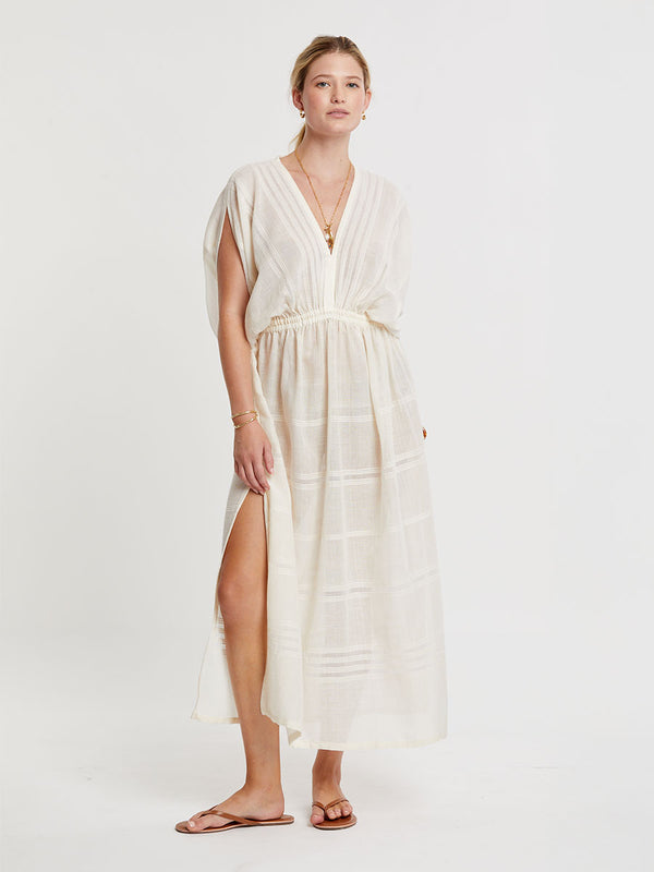 Woman standing wearing lemlem handwoven LEILA Dress featuring extra light gauzy cotton in a delicate cream color.