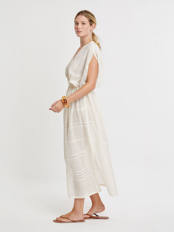 Woman standing wearing lemlem handwoven LEILA Dress featuring extra light gauzy cotton in a delicate cream color.