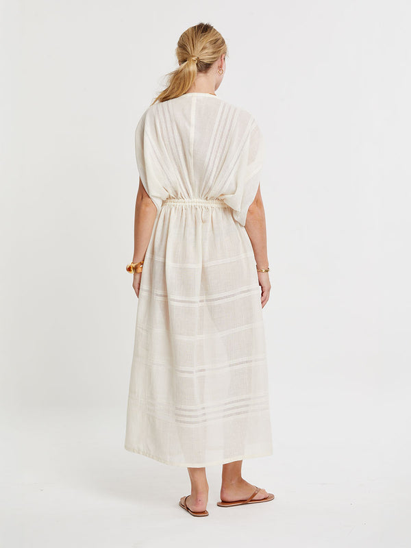 Woman standing wearing lemlem handwoven LEILA Dress featuring extra light gauzy cotton in a delicate cream color.