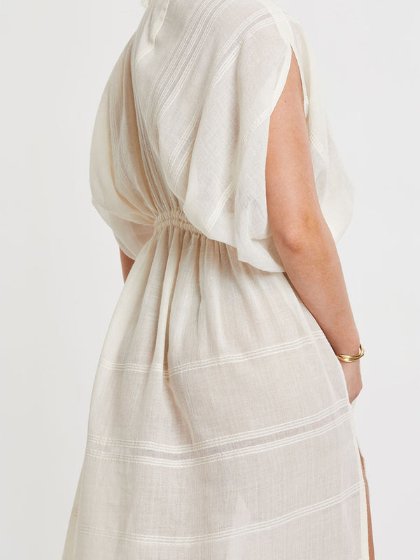 Woman standing wearing lemlem handwoven LEILA Dress featuring extra light gauzy cotton in a delicate cream color.