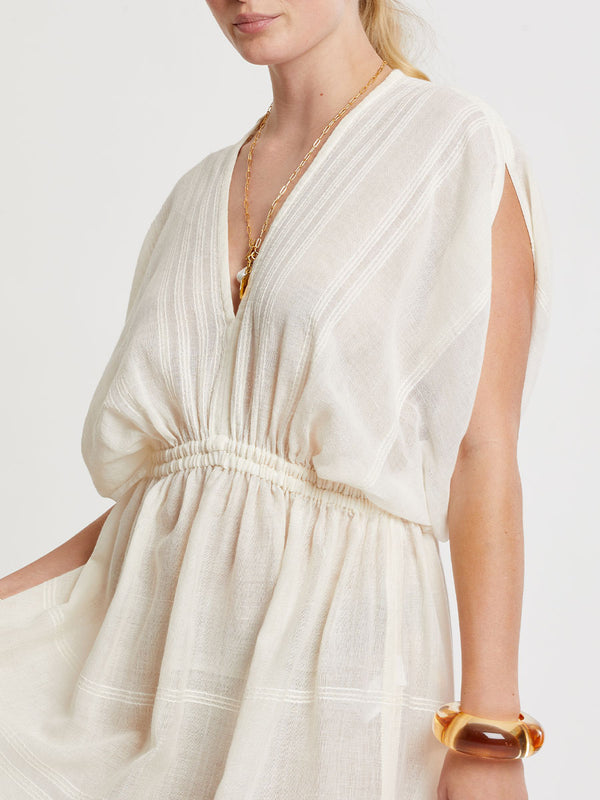 Woman standing wearing lemlem handwoven LEILA Dress featuring extra light gauzy cotton in a delicate cream color.