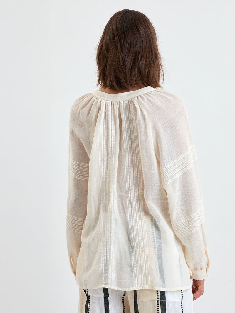 Back of a Woman standing wearing lemlem MITA Handwoven blouse featuring sheer fabric in cream color