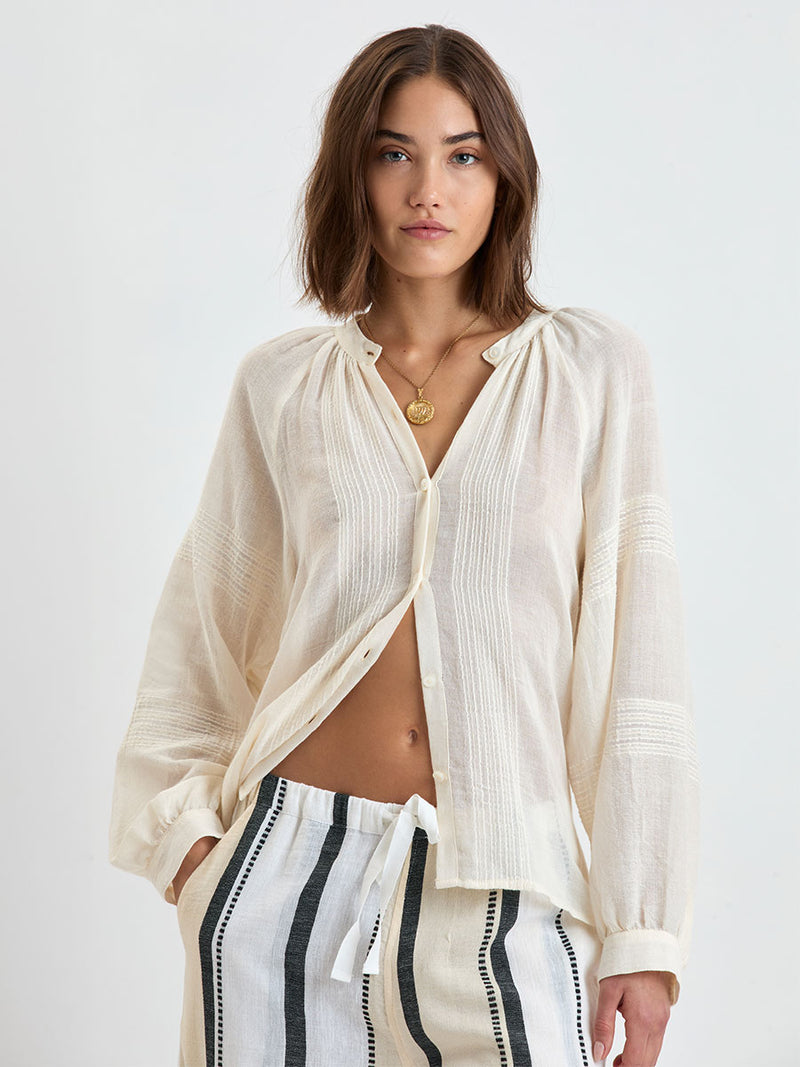 Woman standing wearing lemlem MITA Handwoven blouse featuring sheer fabric in cream color