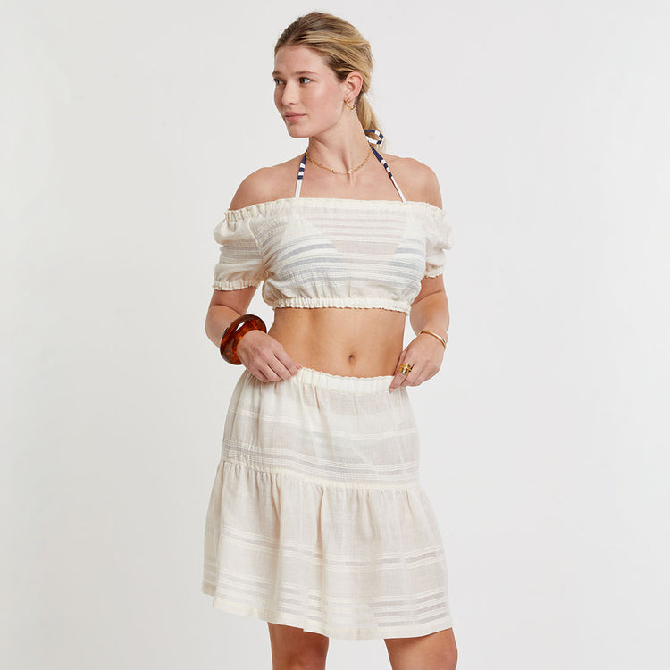 Woman wearing a white off-shoulder lemlem handwoven SOSI  top and skirt on a plain background