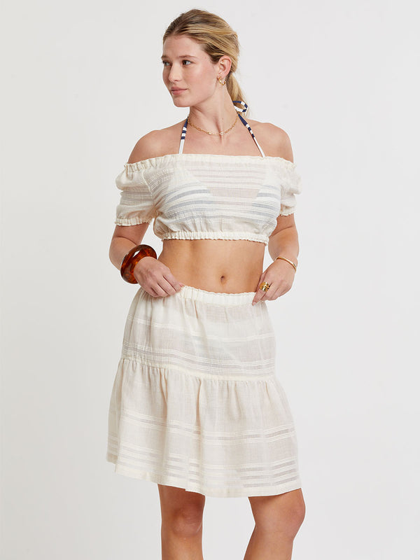 Woman standing wearing lemlem handwoven SOSI Top and CHERI Skirt featuring extra light gauzy cotton in a delicate cream color.