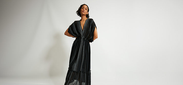 Woman Standing Wearing handwoven  lemlem Leliti Black Dress featuring stiched white pattern on black background 