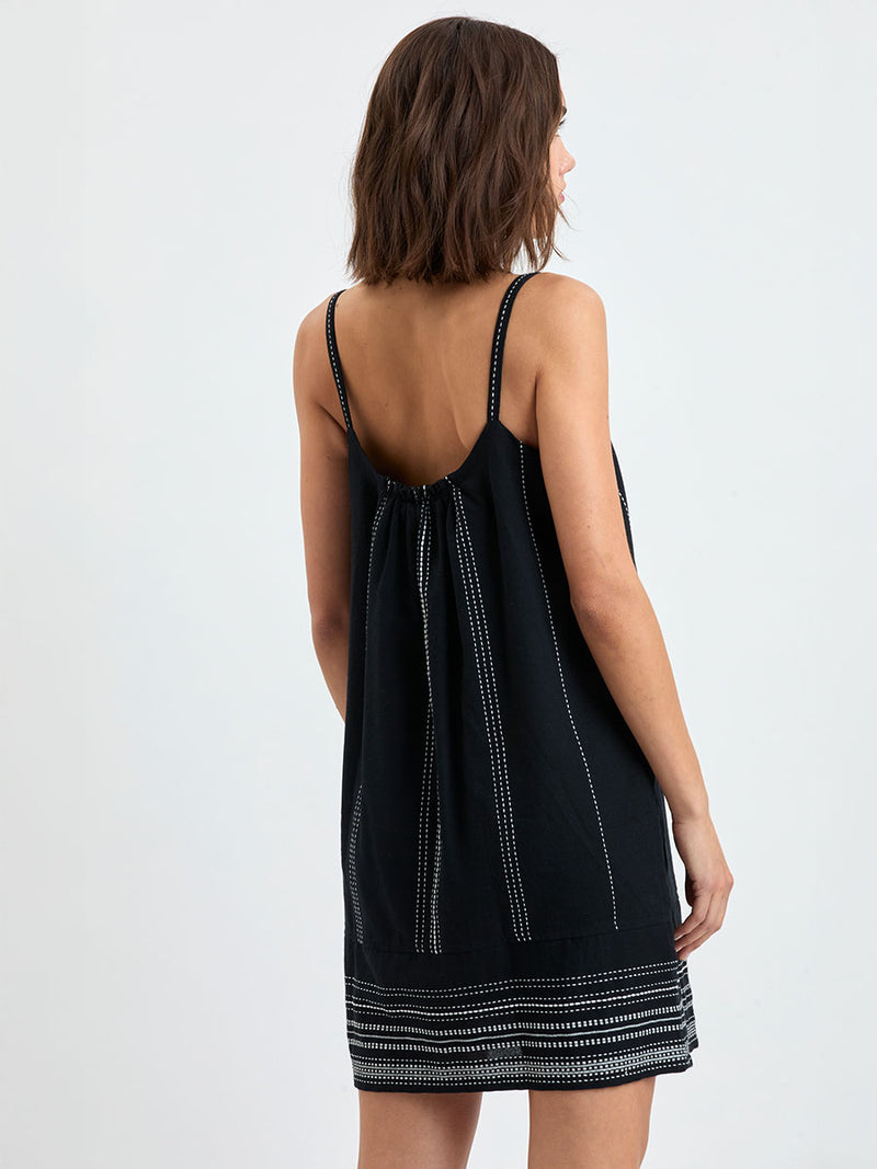 Back of a woman standing wearing lemlem handwoven ZINA Swing Dress dress featuring white dotted pattern in white color on black background