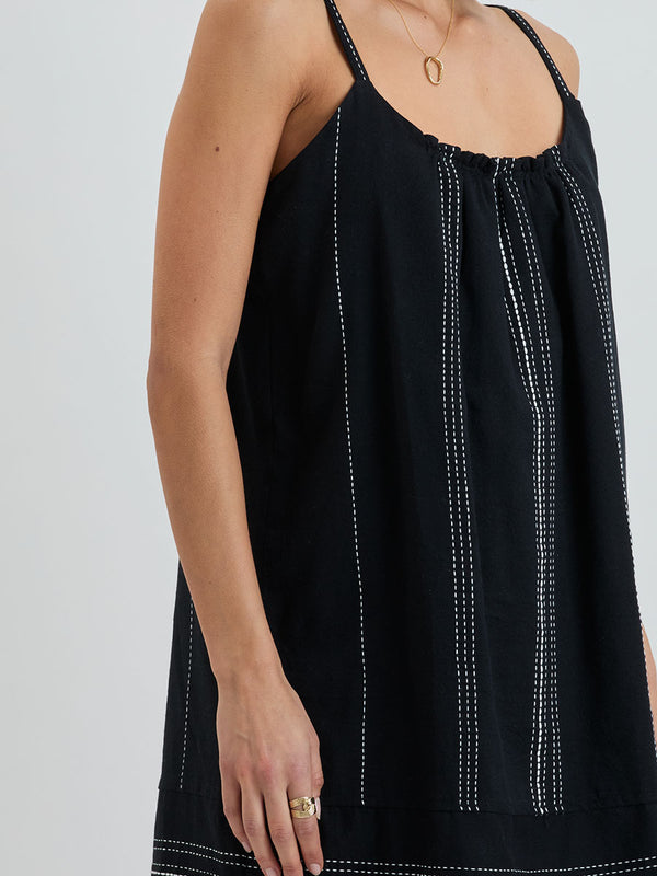 Close up on a woman standing wearing lemlem handwoven ZINA Swing Dress dress featuring white dotted pattern in white color on black background