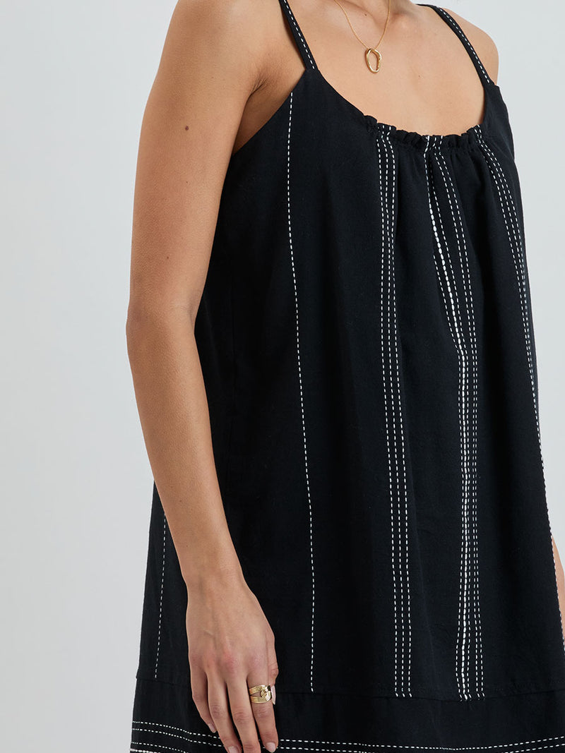 Close up on a woman standing wearing lemlem handwoven ZINA Swing Dress dress featuring white dotted pattern in white color on black background