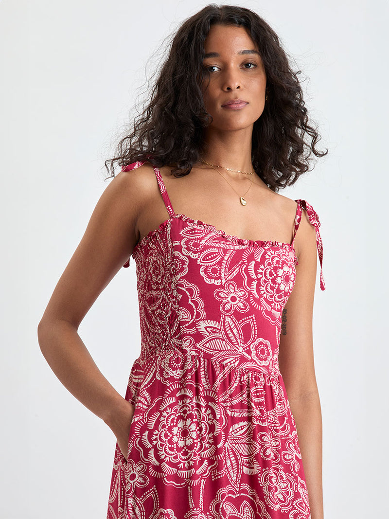 Close up on a Woman Standing Wearing lemlem ANIKA Sundress featuring rich ruby-red fabric  adorned with intricate white floral and leaf motifs print