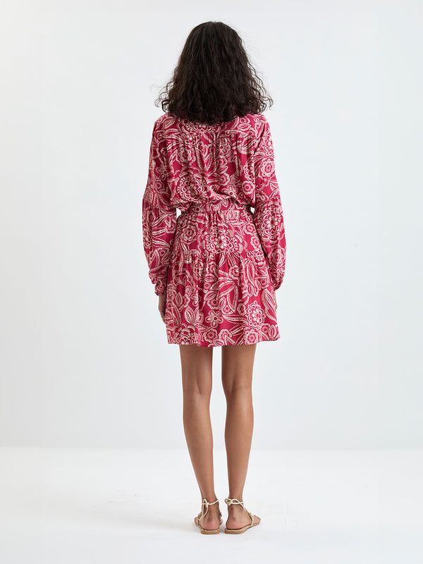 Back of a Woman Standing Wearing lemlem MITA Blouse  and RINA Skirt featuring rich ruby-red fabric  adorned with intricate white floral and leaf motifs print