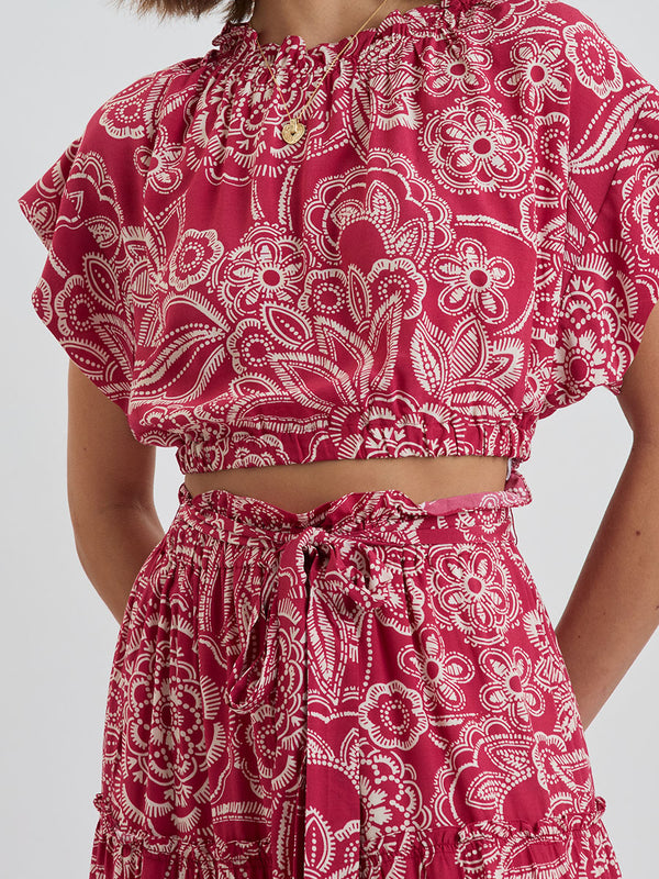 CLose up on a Woman Standing Wearing lemlem MUNA Crop Top and SANAA Skirt featuring rich burgundy fabric with white leaf print