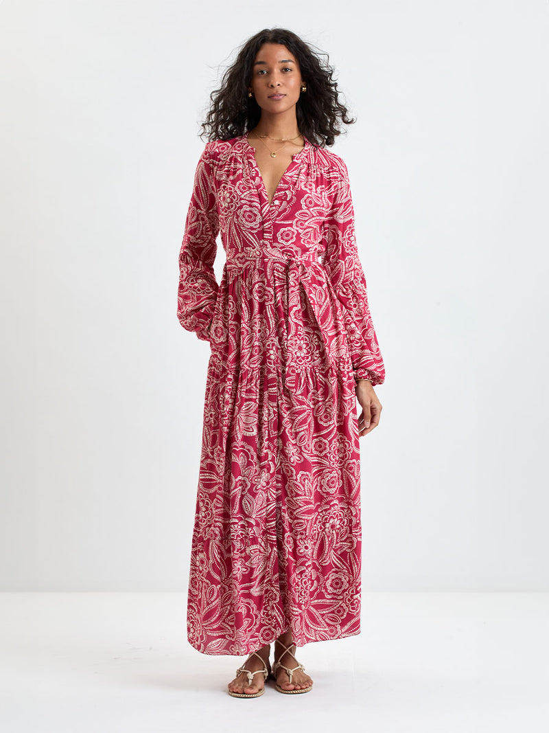 Woman Standing Wearing lemlem NESANET Dress  featuring rich ruby-red fabric  adorned with intricate white floral and leaf motifs print