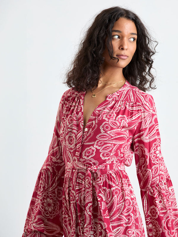 Woman Standing Wearing lemlem NESANET Dress  featuring rich ruby-red fabric  adorned with intricate white floral and leaf motifs print