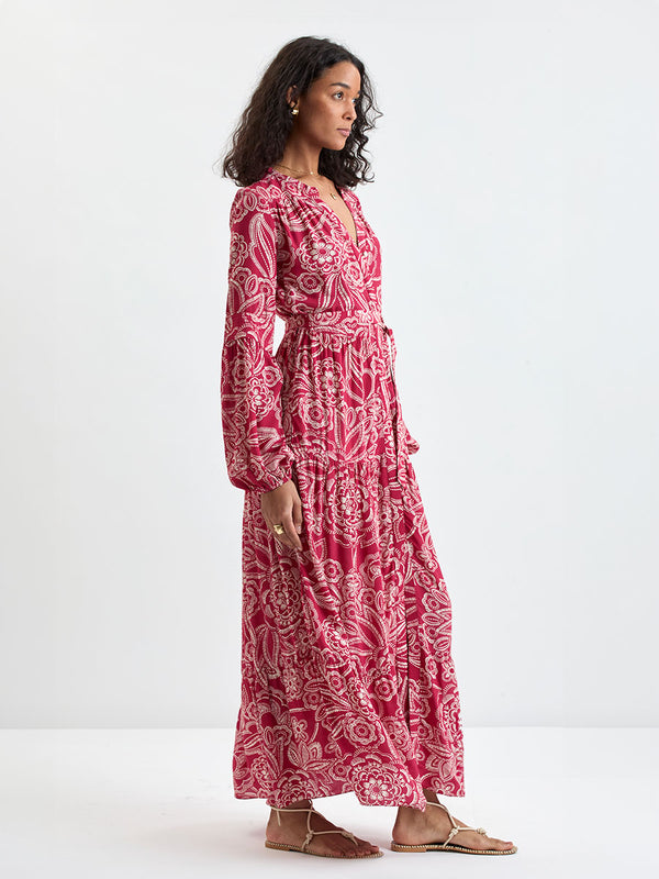 Side shot of a Woman Standing Wearing lemlem NESANET Dress  featuring rich ruby-red fabric  adorned with intricate white floral and leaf motifs print