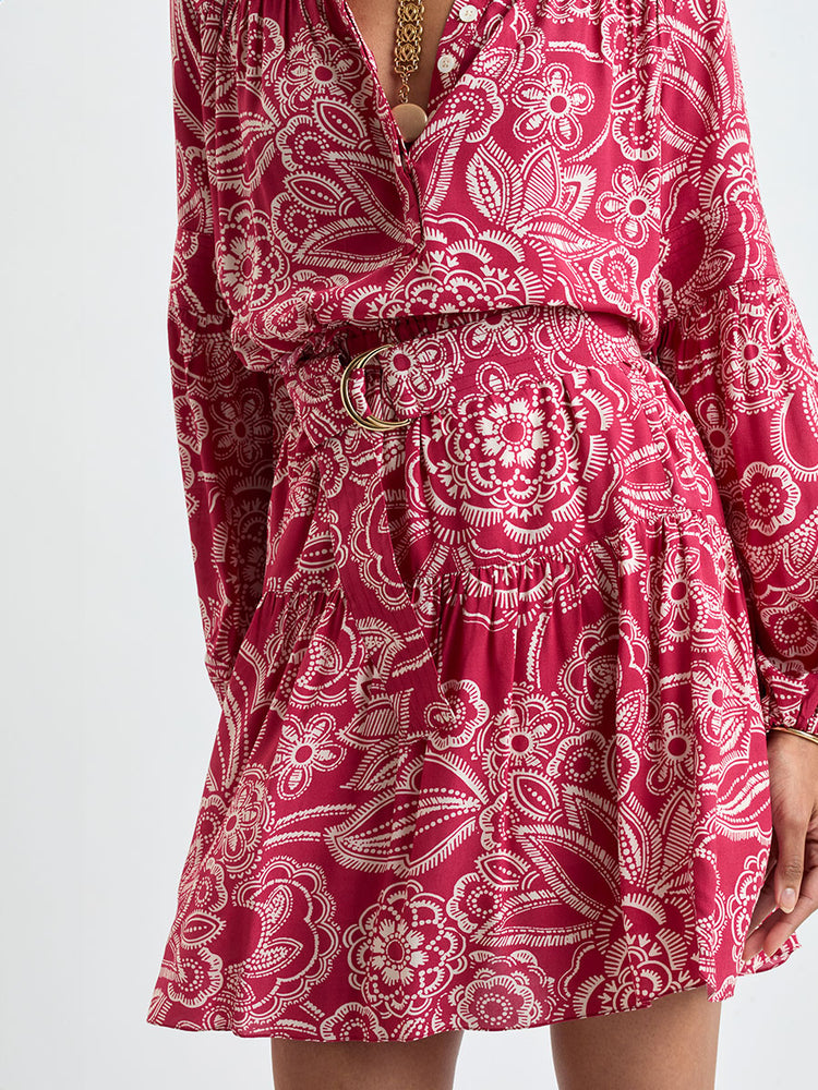 Close up on a Woman Standing Wearing lemlem MITA Blouse  and RINA Skirt featuring rich ruby-red fabric  adorned with intricate white floral and leaf motifs print