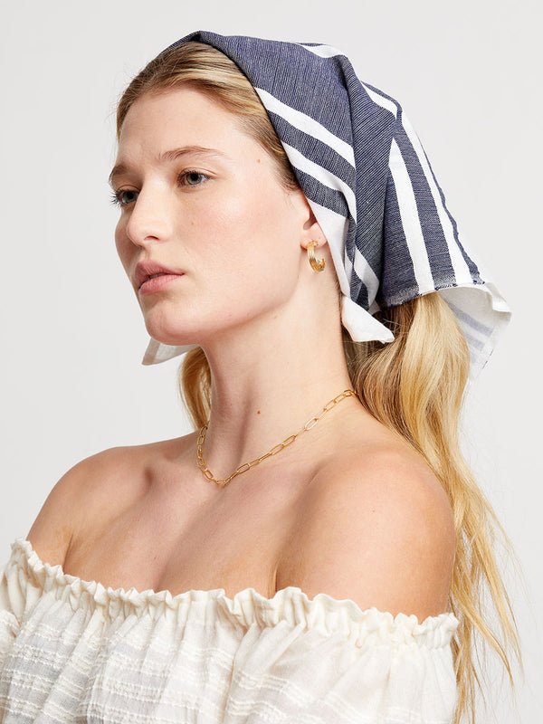 Woman wearing a white off-shoulder top and a striped bandana on a plain background