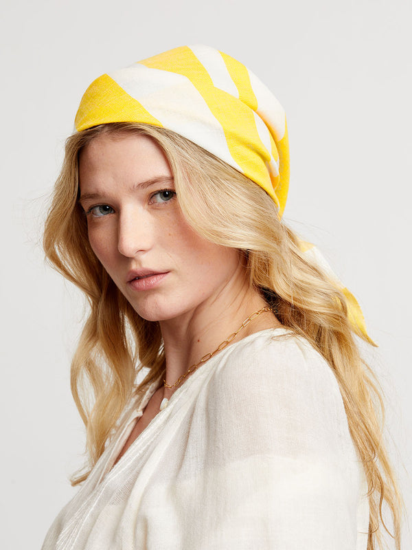 Woman wearing a yellow and white striped bandana on a plain background