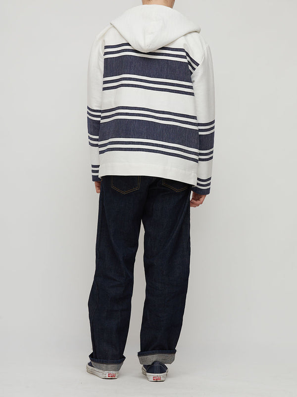 A person shown from the back wearing a white hooded sweatshirt with navy horizontal stripes, paired with dark blue jeans and gray slip-on shoes, against a light gray studio background.